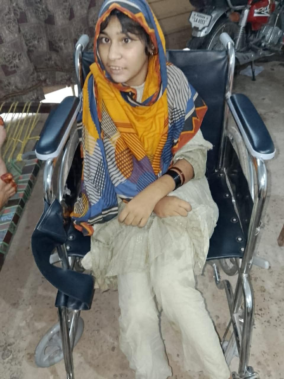 A young girl in a brightly patterned scarf seated in her wheelchair.